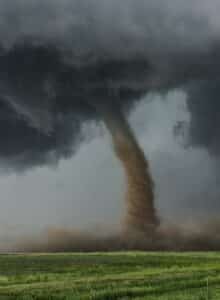 Dark tornado and clouds sweeping through a field.