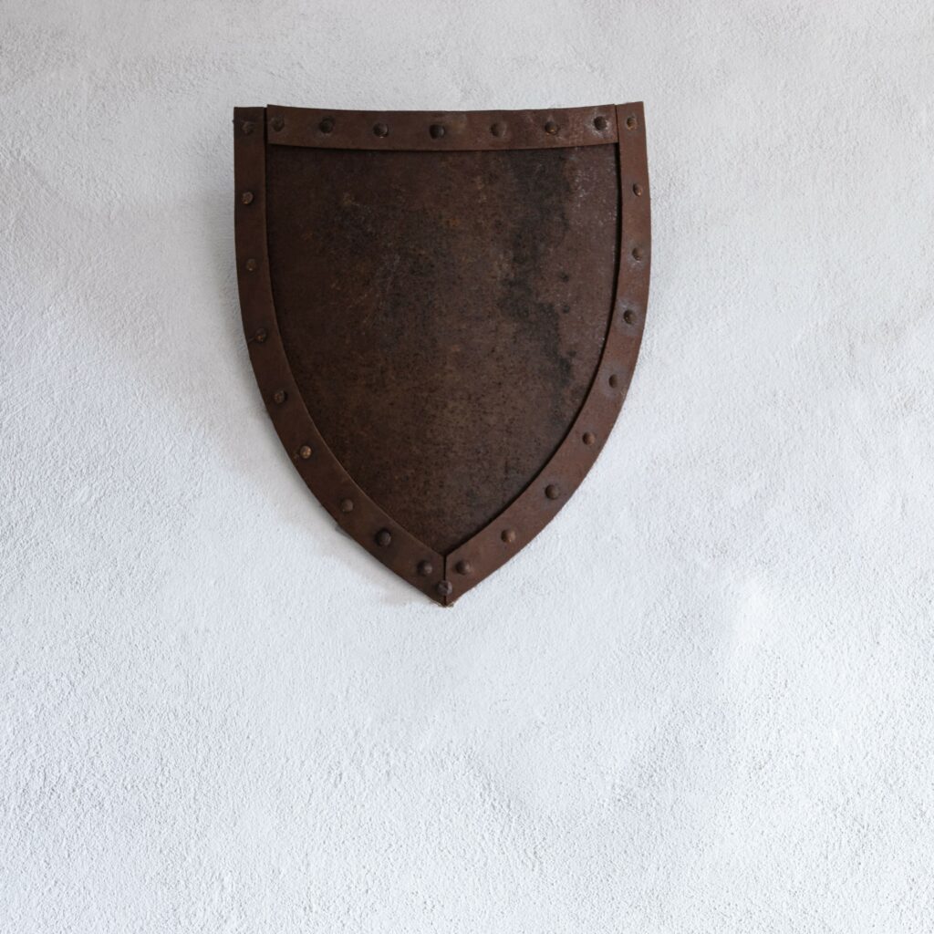 Metal, medieval shield hung up on a white wall.