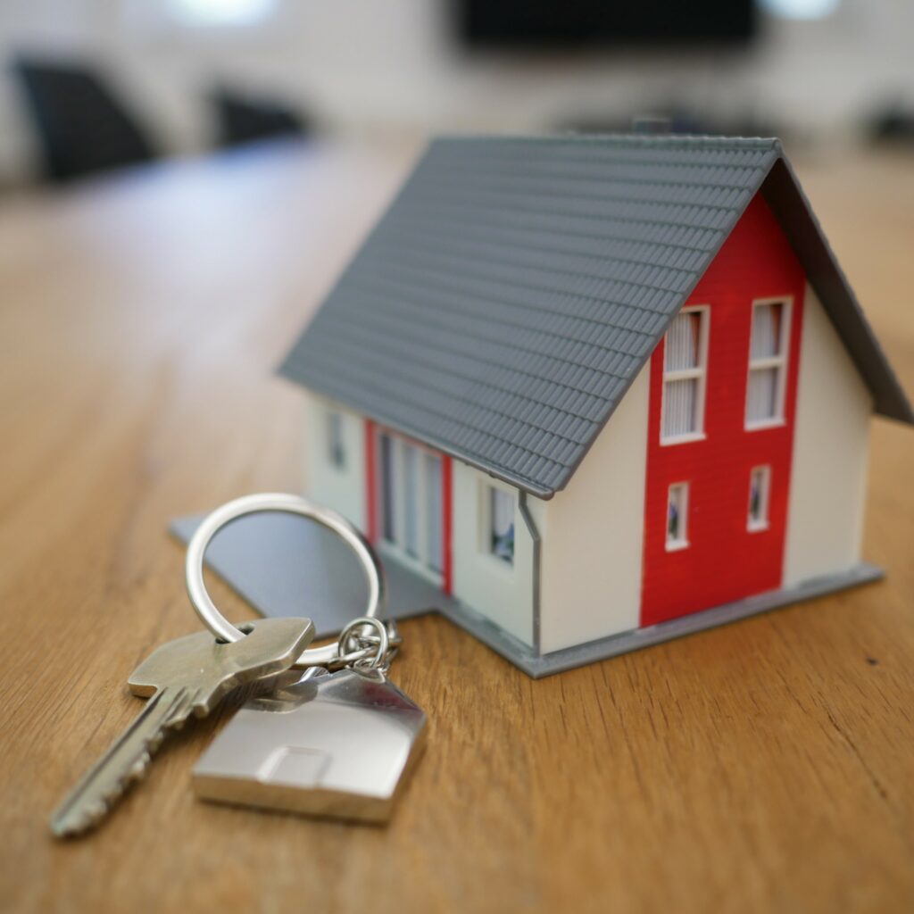 Miniature toy red and white home on a table next to a set of house keys.