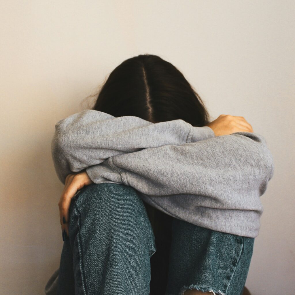 Woman with dark hair sitting on the floor with her arms around her face, as if crying about an unfortunate claims handling experience.