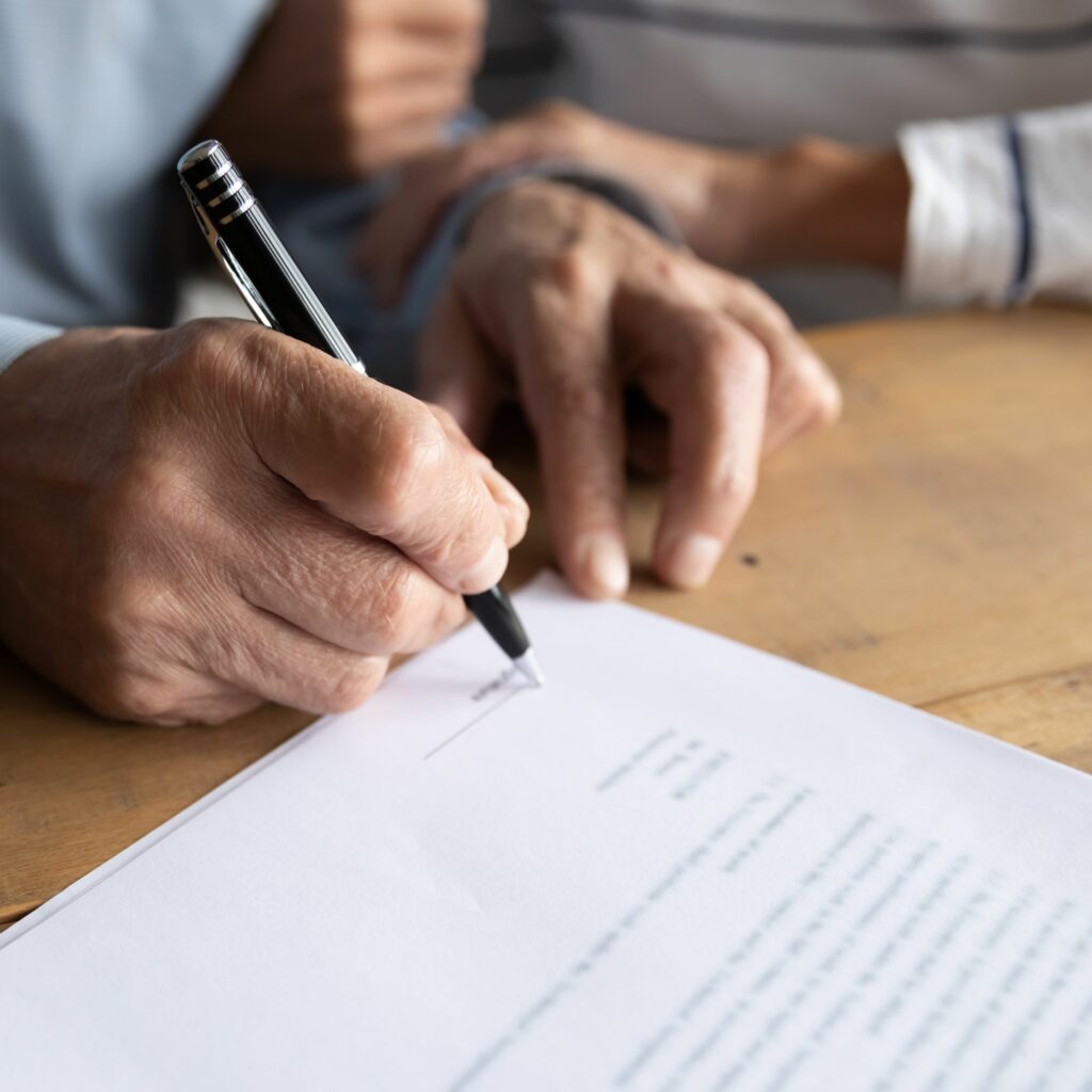 Close-up of man and woman's hands as man holds a pen to sign a printed home inspection contract.