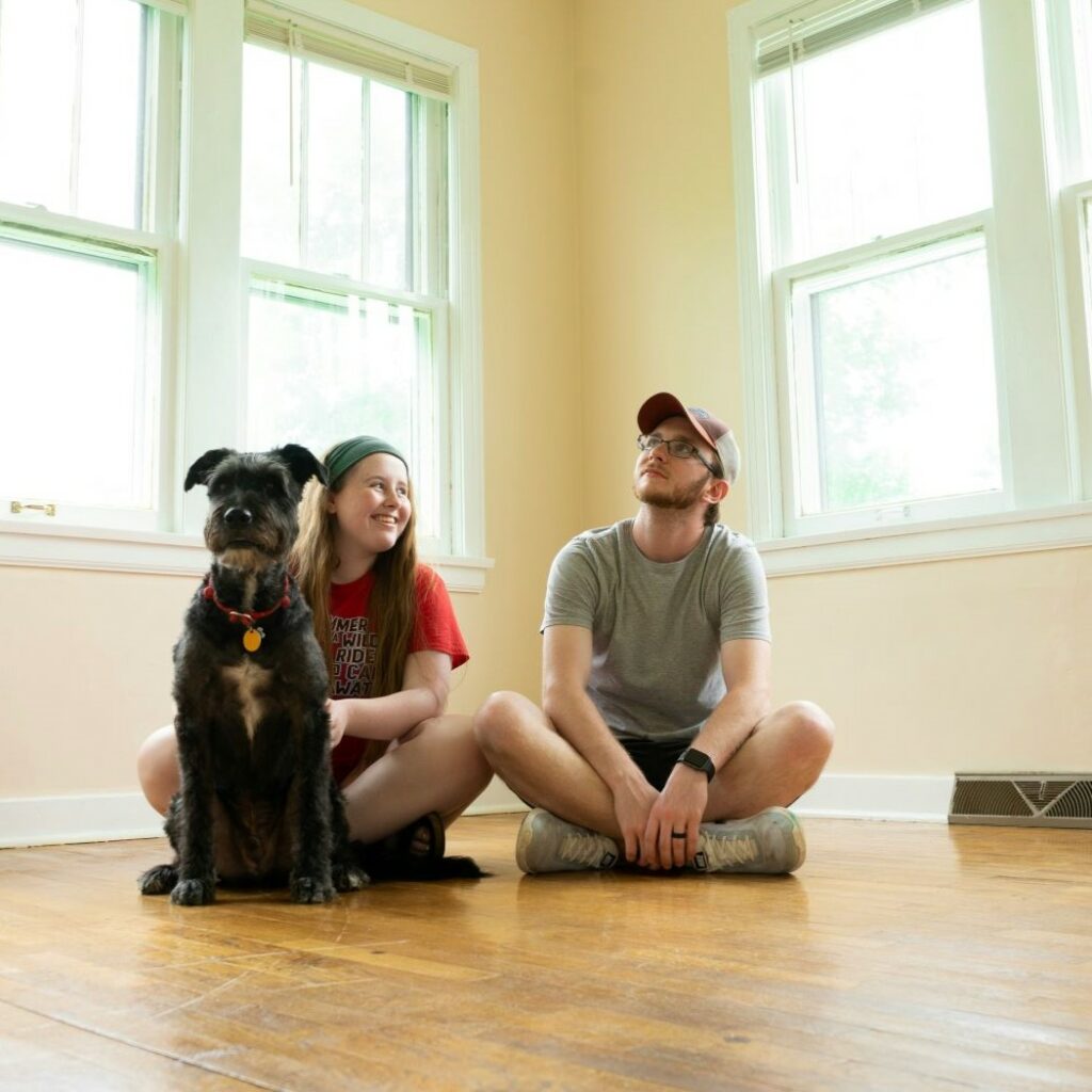 Young man and woman with dog sitting in empty room, presumably after moving into a new home.