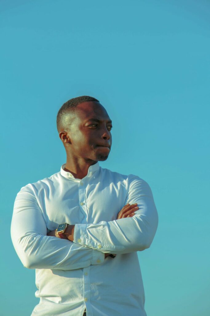 Man in collared white shirt standing with arms folded and looking away from the camera.