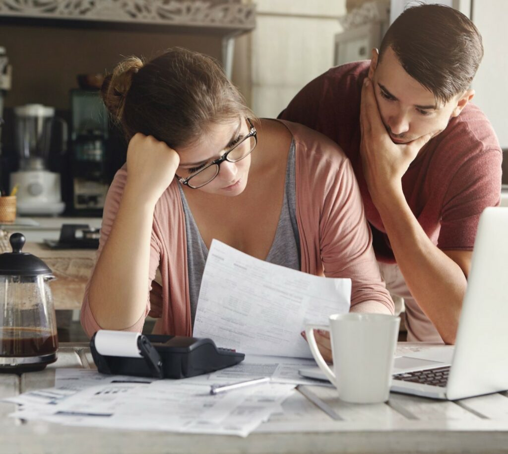 Man and woman at kitchen table with laptop, papers scattered, coffee, and calculator as if calculating insurance premium increases. One of the common myths about insurance premiums is that reporting claims automatically means higher premiums. 