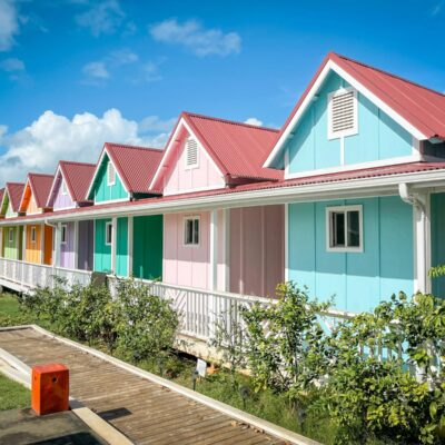 Seven pastel-colored tiny houses surrounded by green grass and a bright, blue sky in Hawaii.