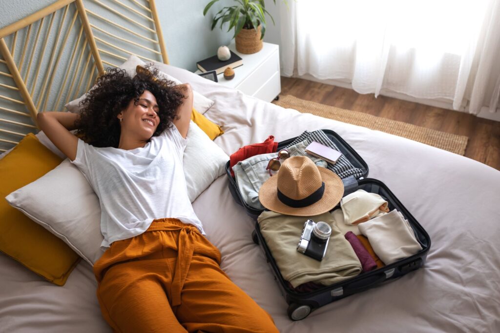 Woman relaxing on a bed at a hotel or vacation rental home with her suitcase open next to her.