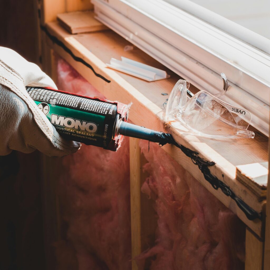Worker applying sealant to a window of a new house in a sloppy way, which is a common new construction cosmetic issue.
